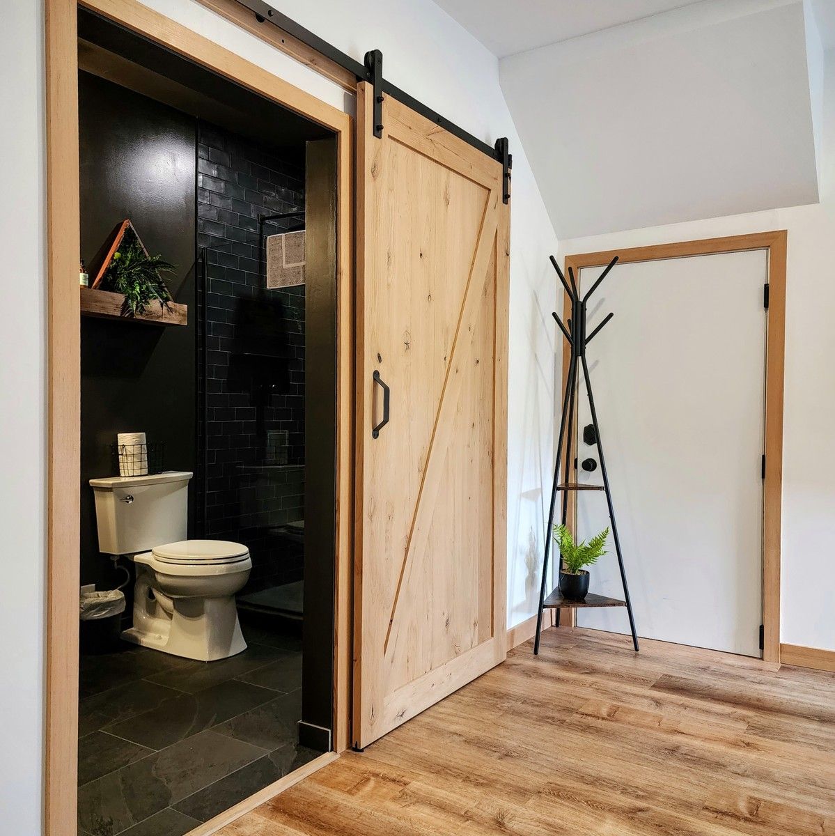 Converted garage suite in Ucluelet, with a wood barn door open to a dark-tiled bathroom.