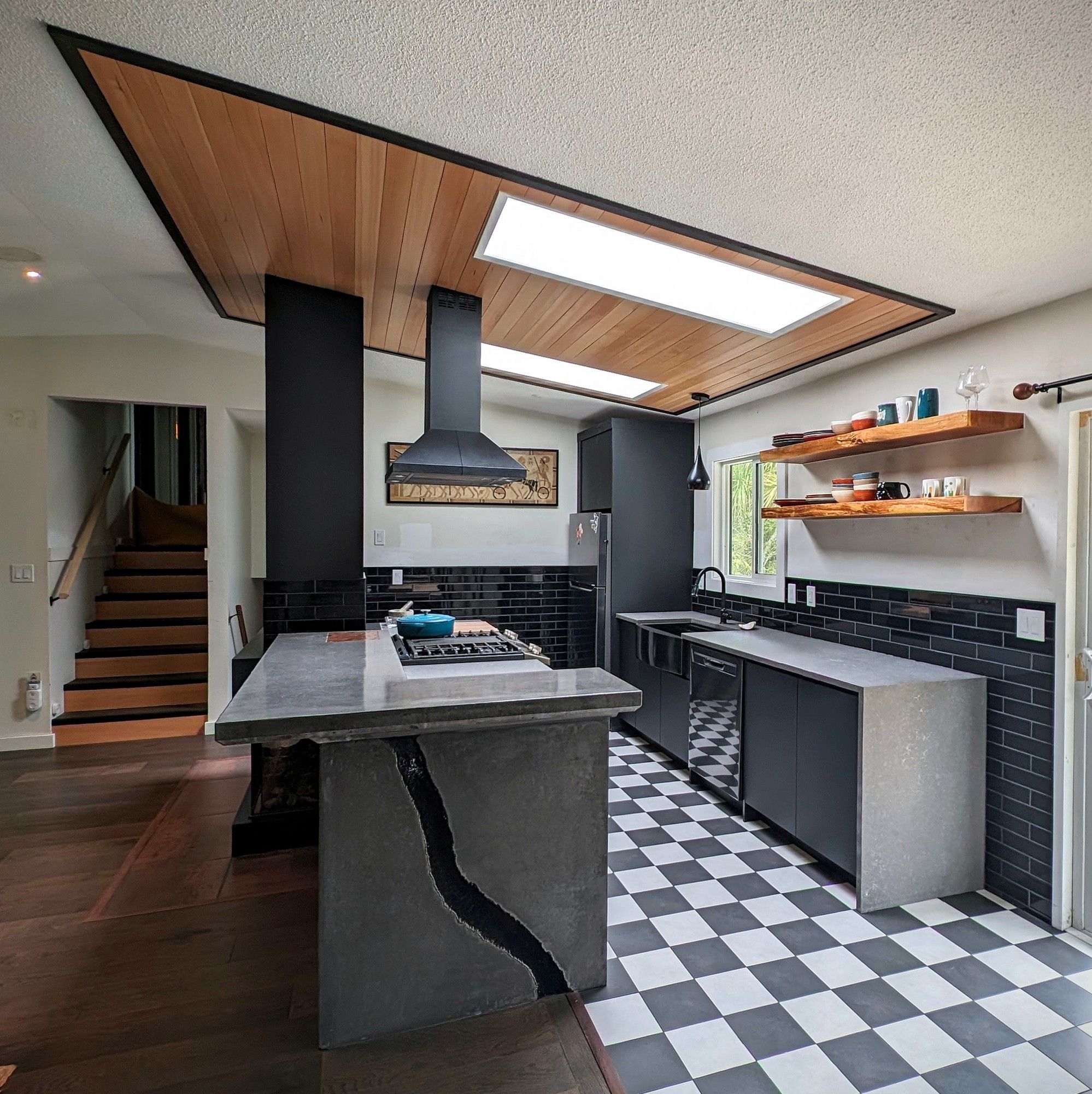 Finished kitchen in Ucluelet with a fir ceiling, skylights, a concrete island and a checkered tile floor.